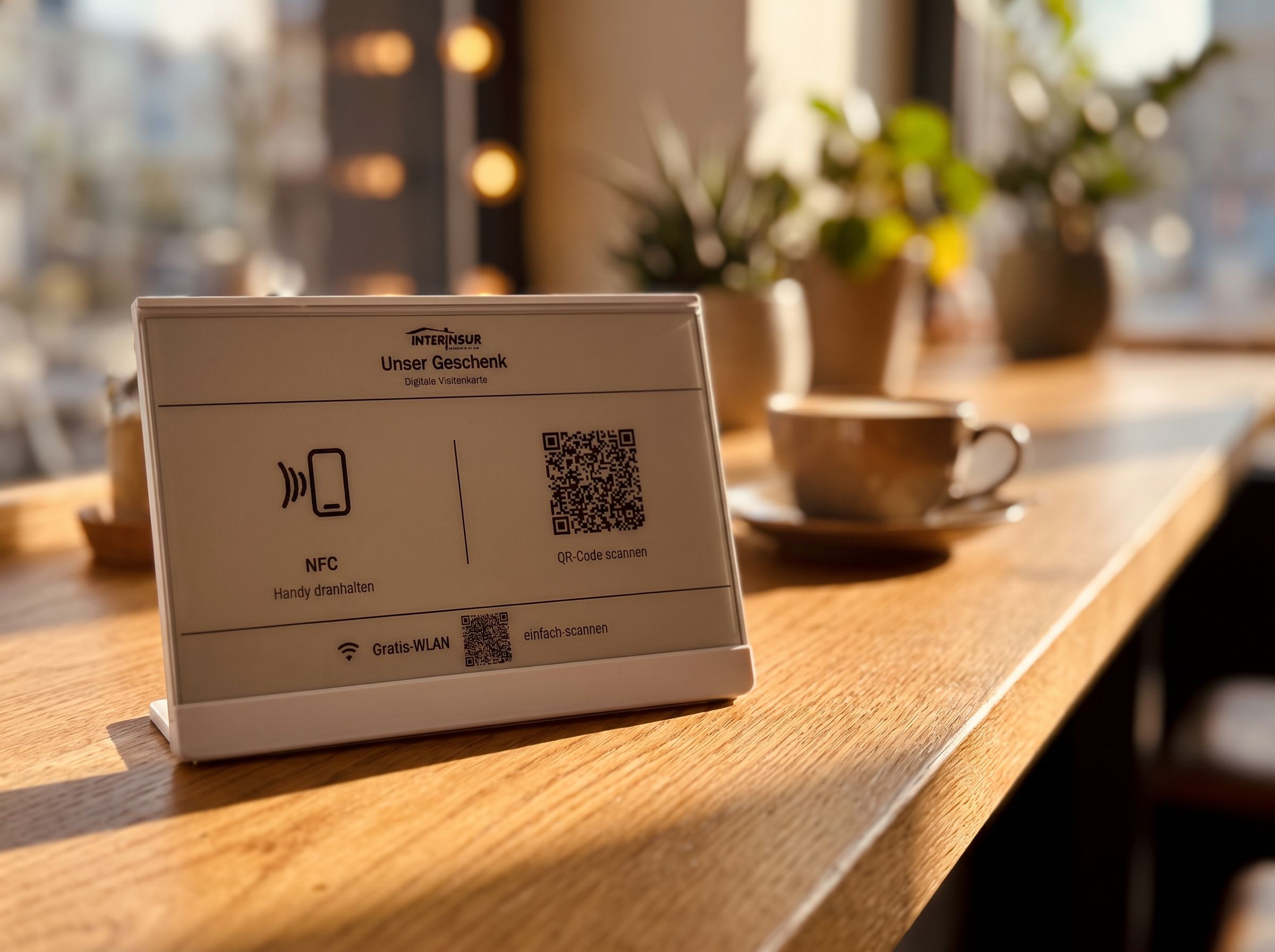 Das Landingdisplay auf einem warmen Holztresen im Abendlicht: E-Paper-Aufsteller mit NFC-Zone, QR-Code und Gratis-WLAN